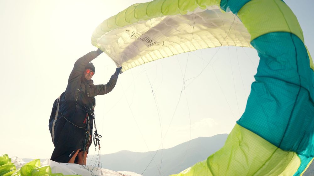 A paraglider prepares their colorful green and white canopy against a bright sky backdrop.