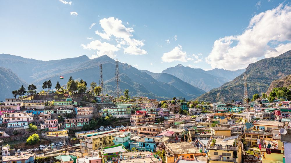 Colorful hillside town with vibrant buildings nestled among lush green mountains under a bright blue sky.