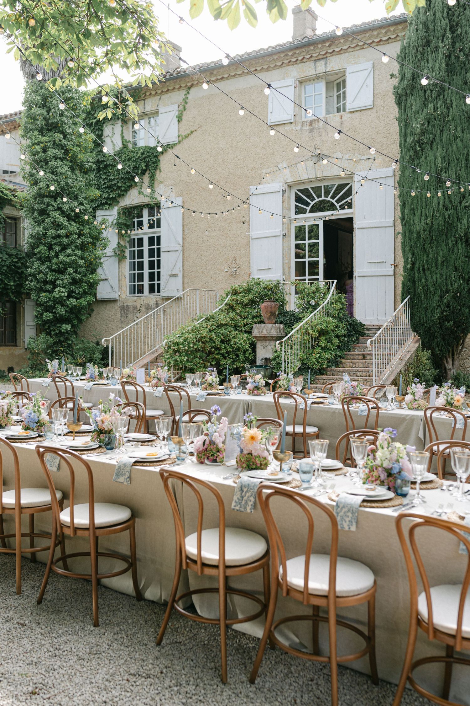 Elegant outdoor wedding reception with long tables, floral centerpieces, and string lights at a French chateau. - Chateau de Lartigolle
