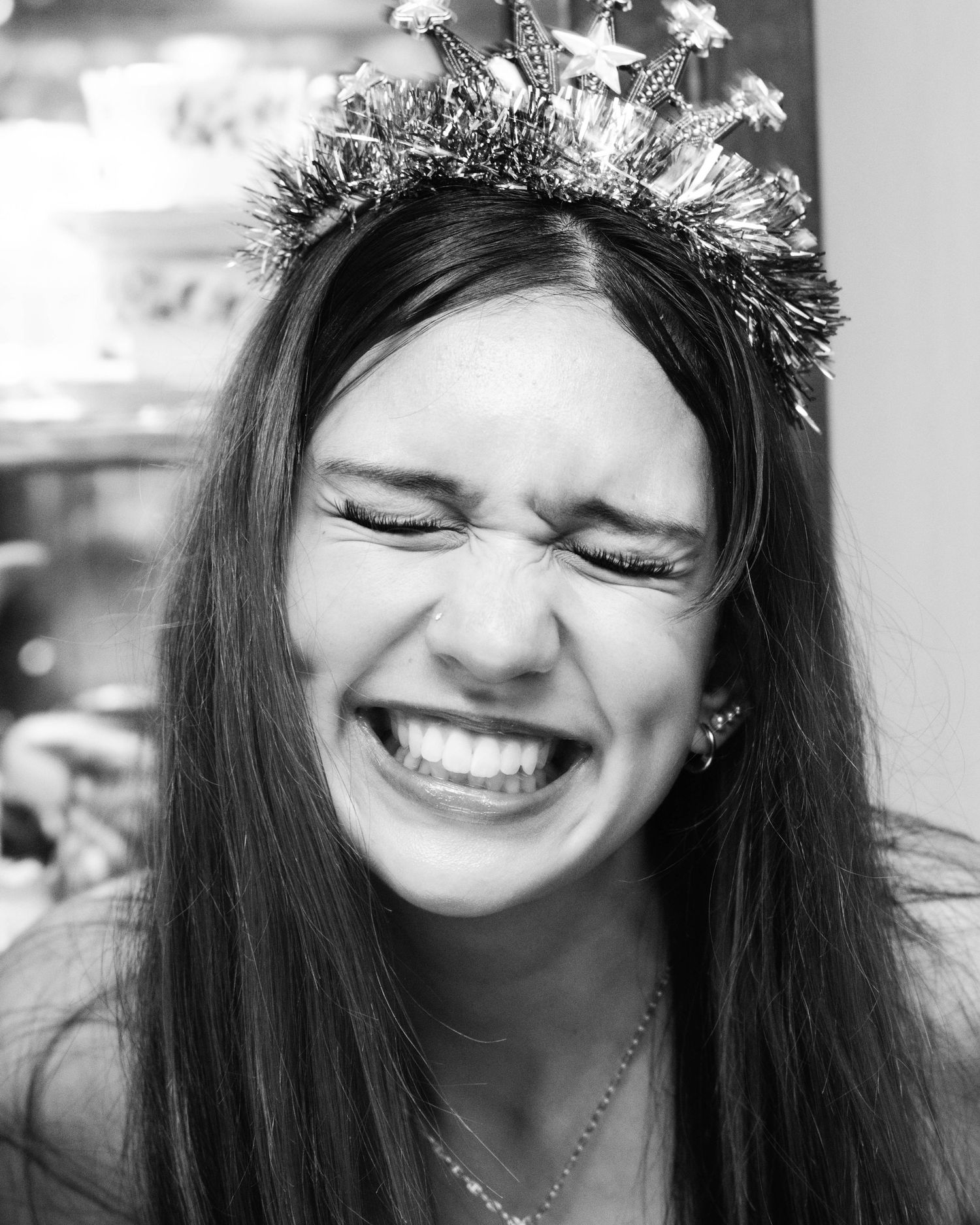 Black and white photo of a laughing young woman wearing a festive star crown headband with eyes closed.