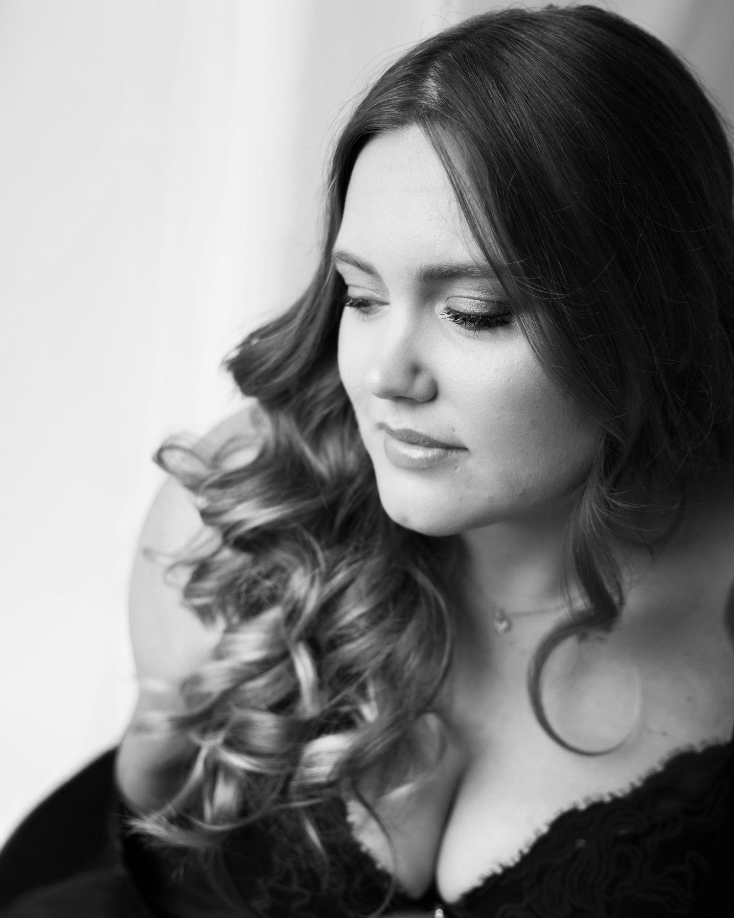 Black and white portrait of a young woman with curly hair looking down gracefully.