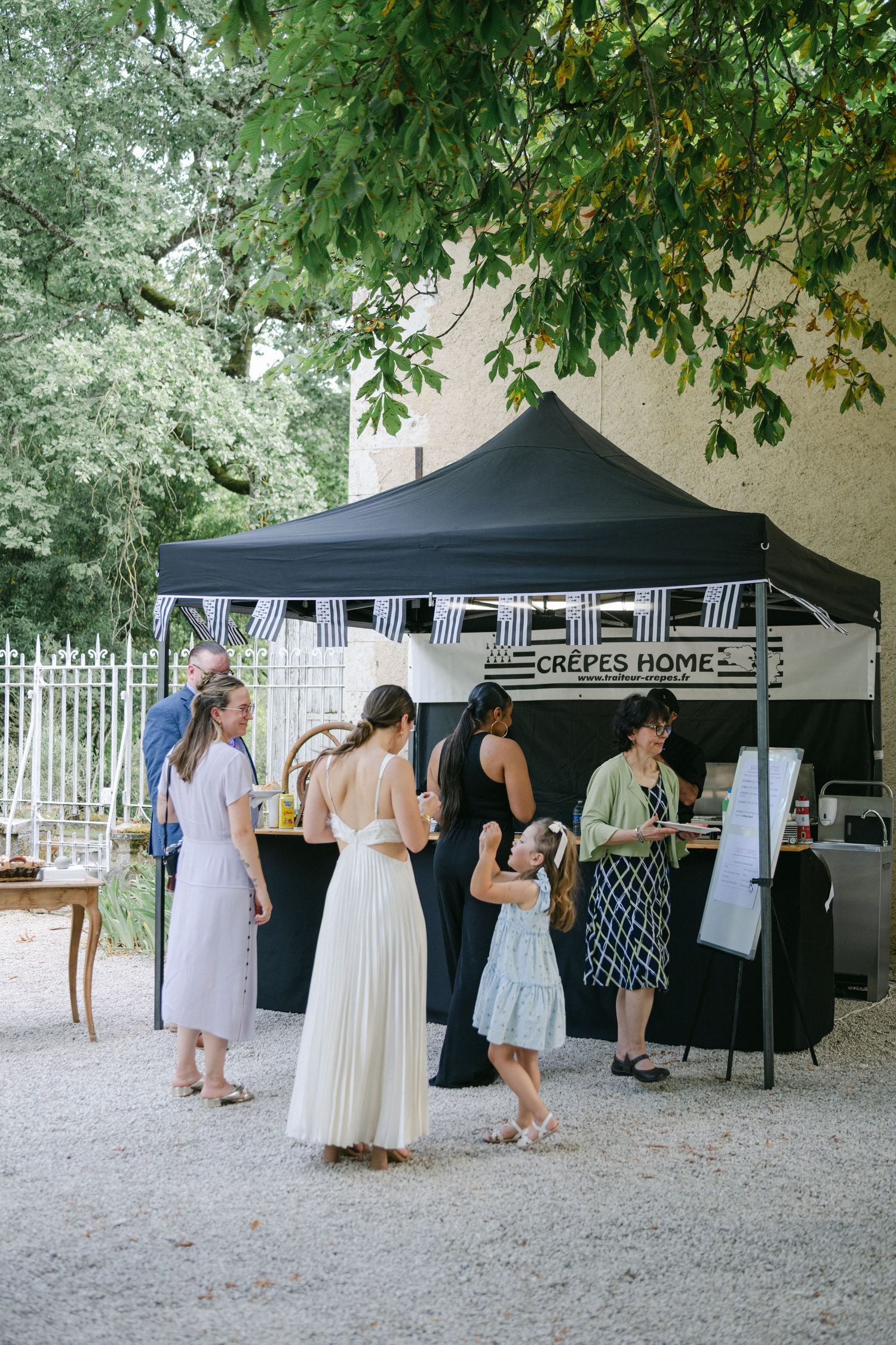 Guests gather at a Crepes Home food stall under a black canopy tent at an outdoor wedding reception.