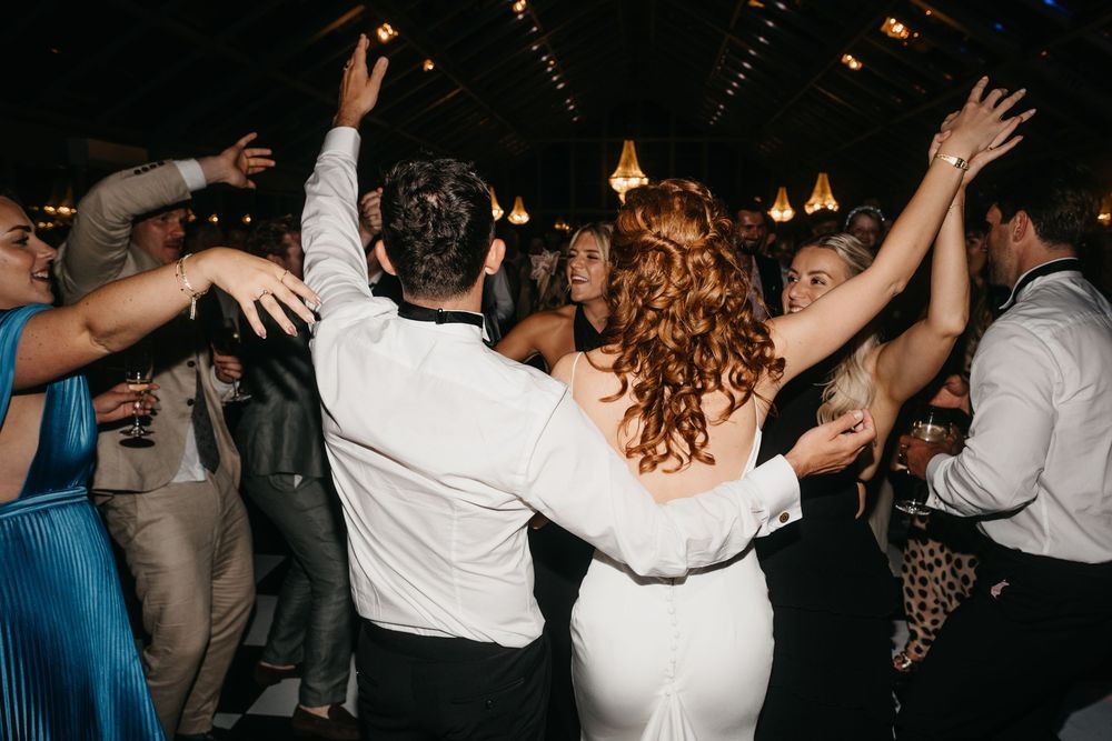 Bride and groom dancing joyfully with wedding guests on a crowded dance floor at a lively reception.