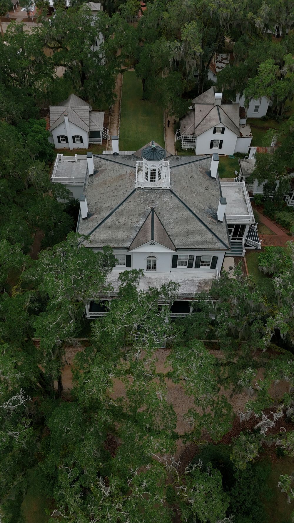 Aerial drone view of a historic Southern plantation home surrounded by lush moss-draped trees.