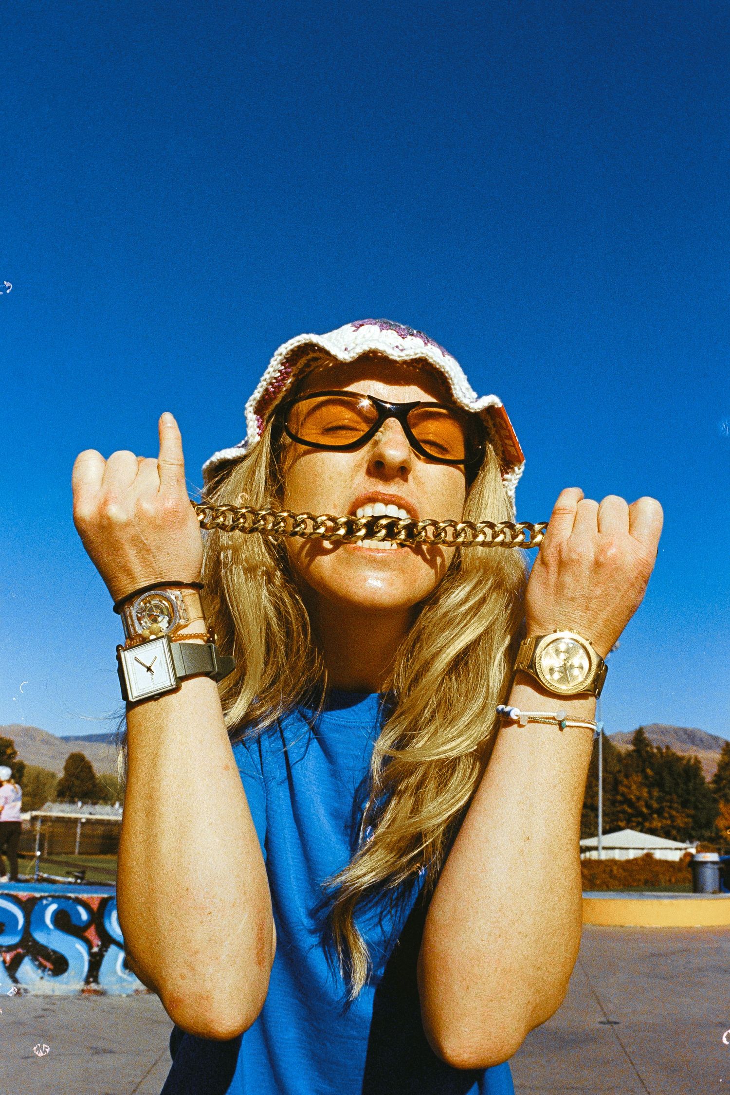 Casey Brown in sunglasses and beanie making rock hand gestures against blue sky.