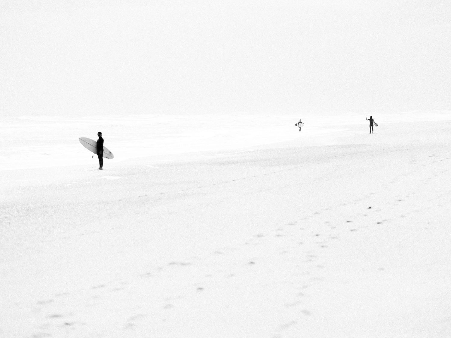 Minimalist beach landscape with distant figures carrying surfboards on snowy beach.