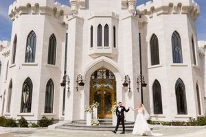 Bride and groom celebrating outside a stunning white castle wedding venue with Gothic arched windows and ornate doors.
