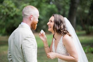 Bride laughing and feeding groom wedding cake outdoors at a garden wedding ceremony.