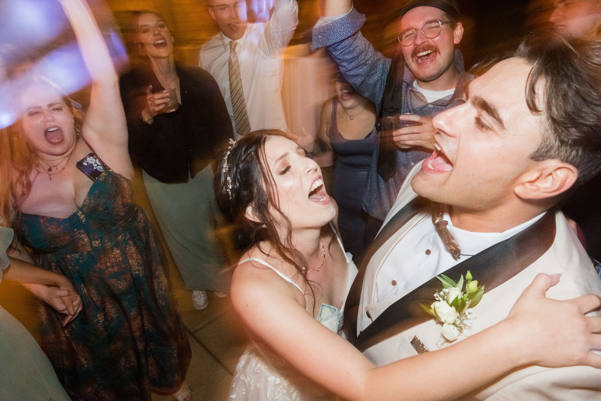 Joyful bride and groom dancing at wedding reception surrounded by celebrating guests.