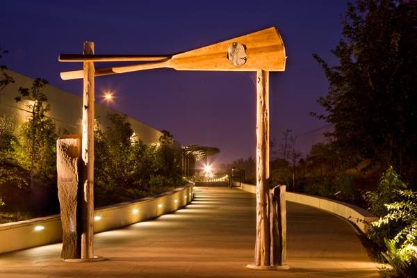 Illuminated wooden paddle gate arch over a winding pathway at night, surrounded by lush greenery and warm lights.
