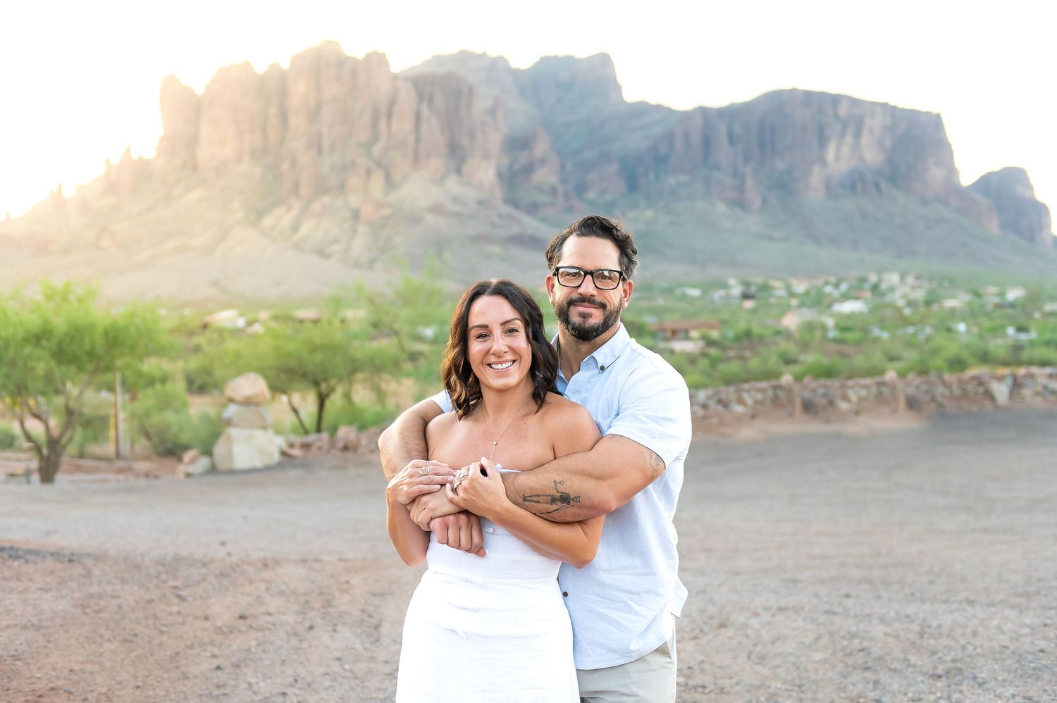Couple on vacation in Arizona celebrating their anniversary standing in front of the Superstition Mountains at Goldfield Ghost Town.
