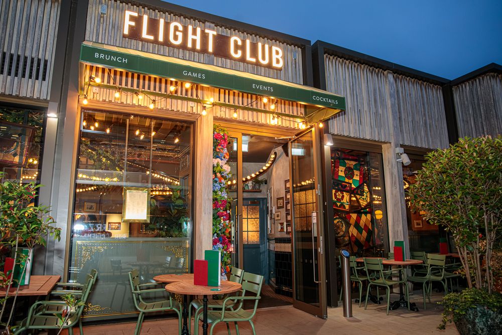 Flight Club bar exterior at dusk with festive lighting and outdoor seating.