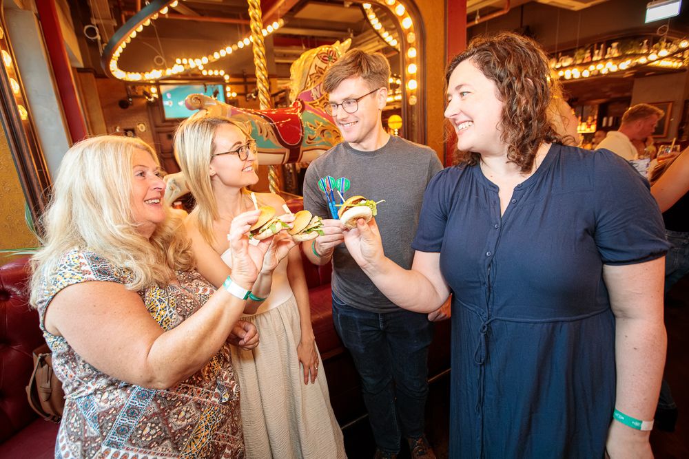 Four people smiling and sharing food at a colorful restaurant, enjoying appetizers together in a lively dining setting.