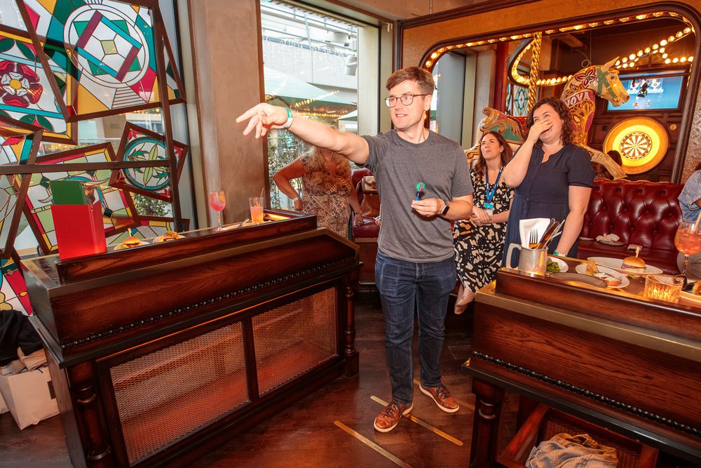 Man playing a game at a colorful arcade bar with stained glass windows and friends watching.