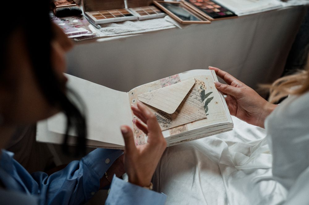 Two people examining a decorative envelope with pressed leaves in an open scrapbook album.