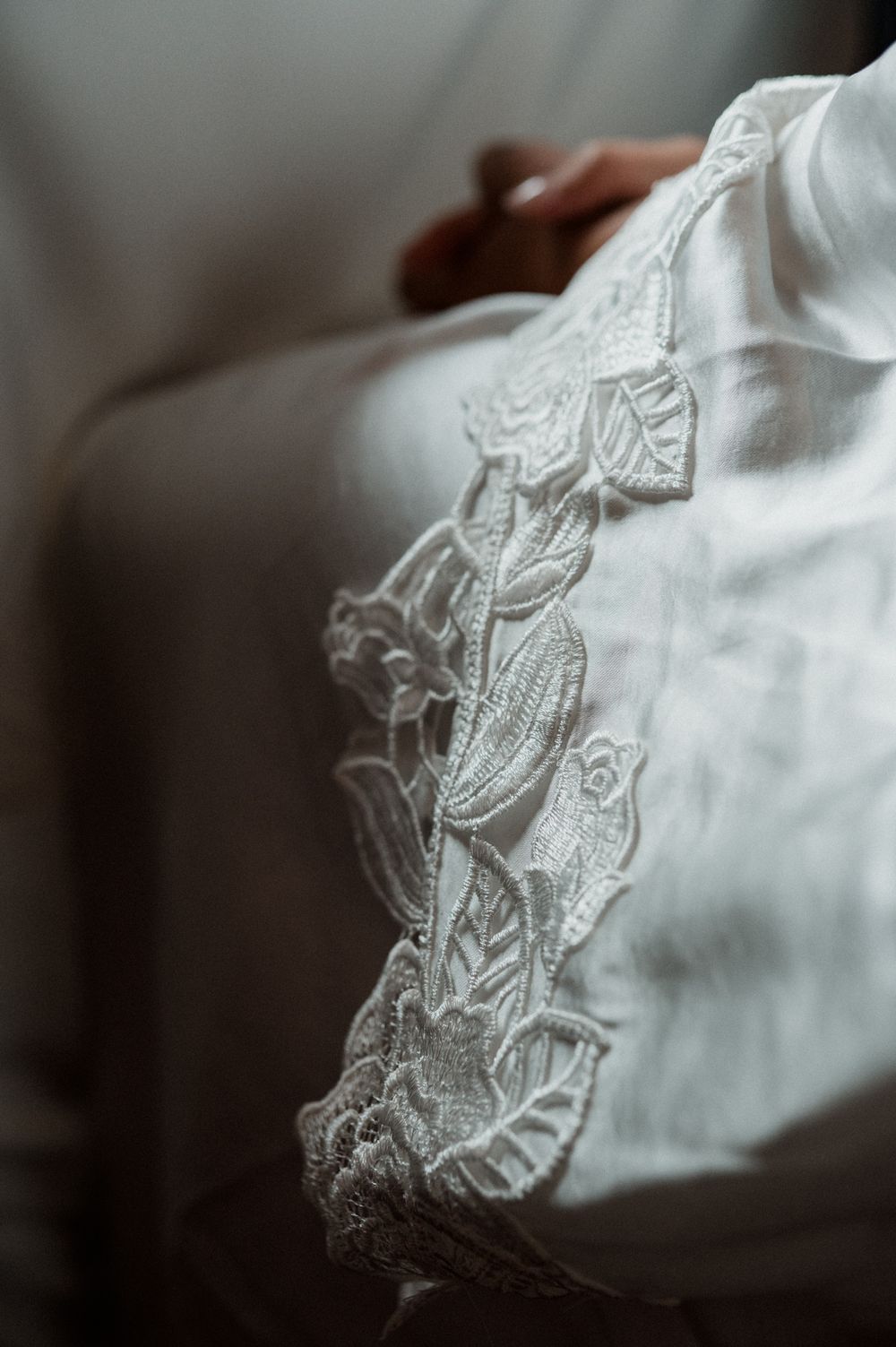 Close-up of delicate white lace floral embroidery on a bridal gown sleeve, with soft bokeh background.