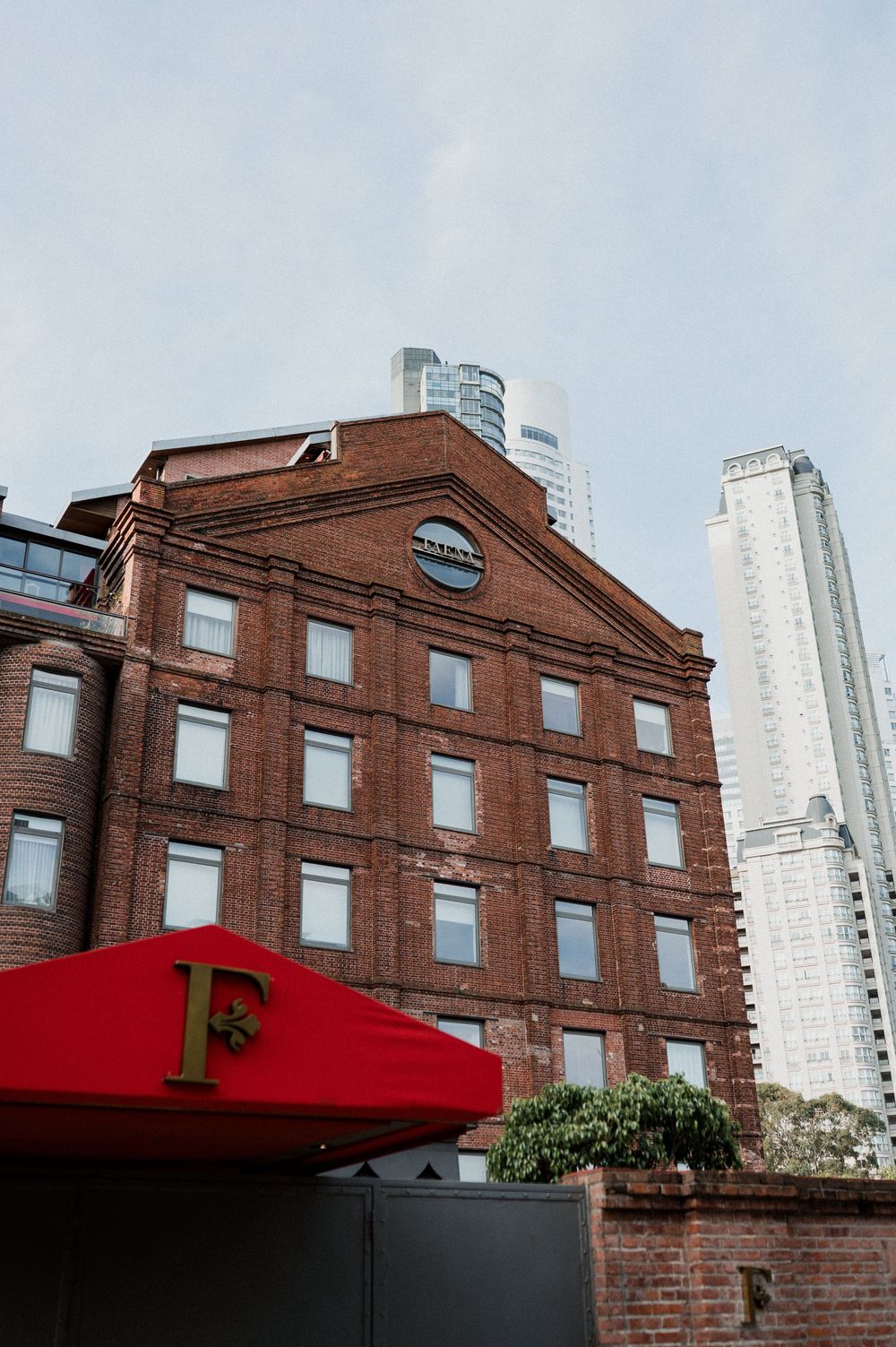 Historic red brick building with modern skyscrapers behind it, featuring a red awning with gold letter F at entrance.