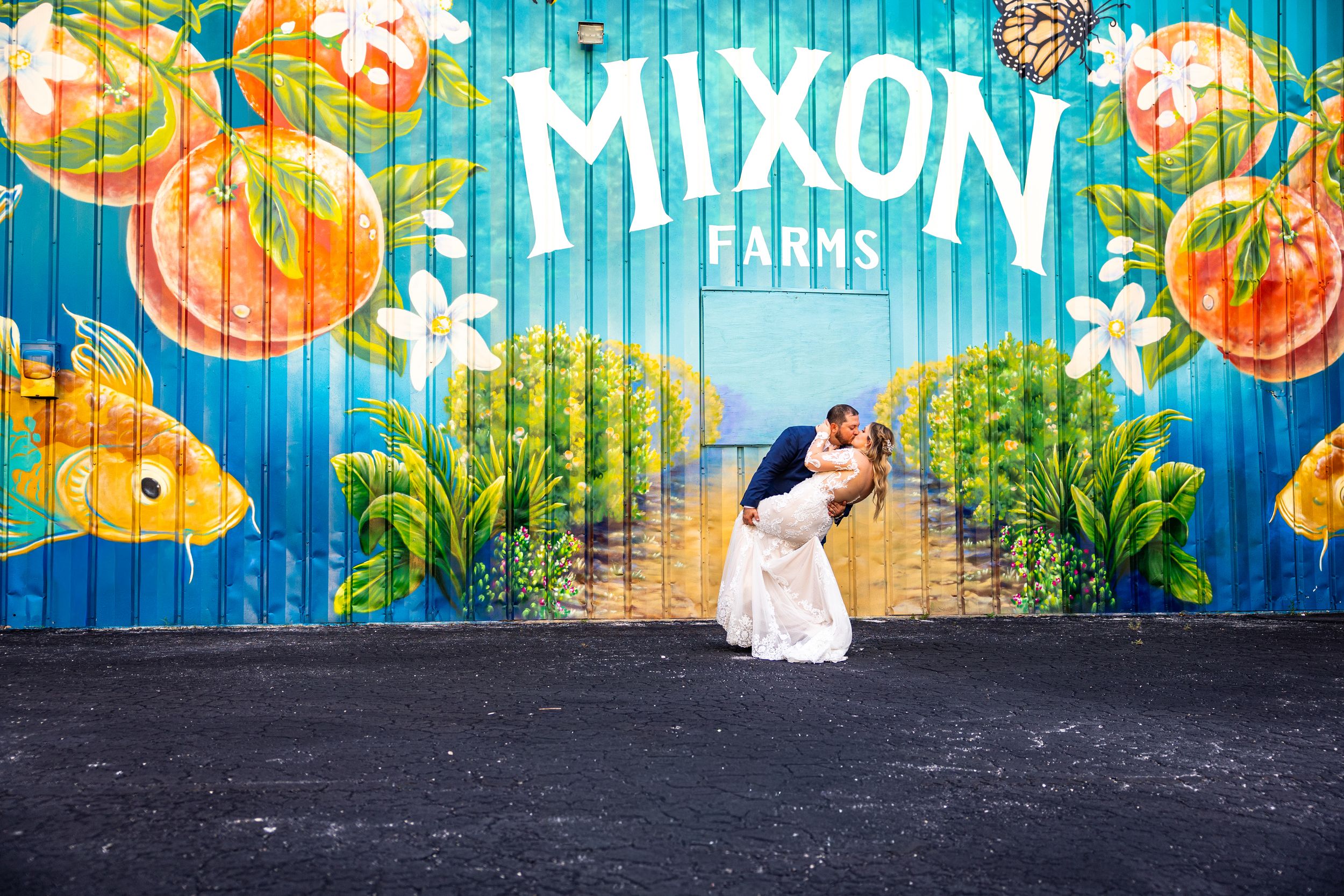 Bradenton Fl wedding pictures ofCouple sharing a romantic dip kiss in front of colorful Mixon Farms mural with oranges and tropical foliage.