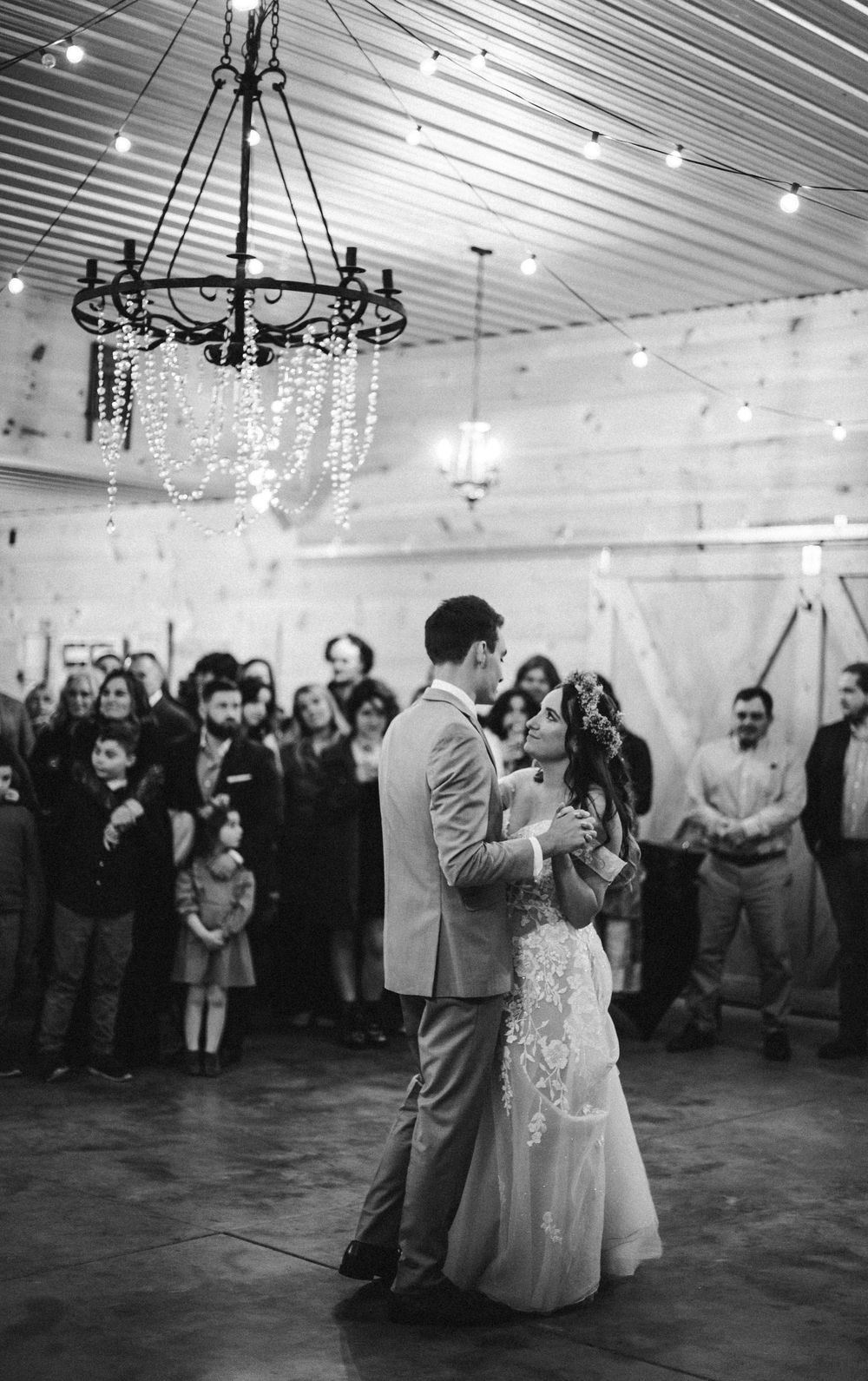 A black and white wedding reception first dance under a rustic chandelier at The Barn at Young Harris venue by Ella Monroe Photography