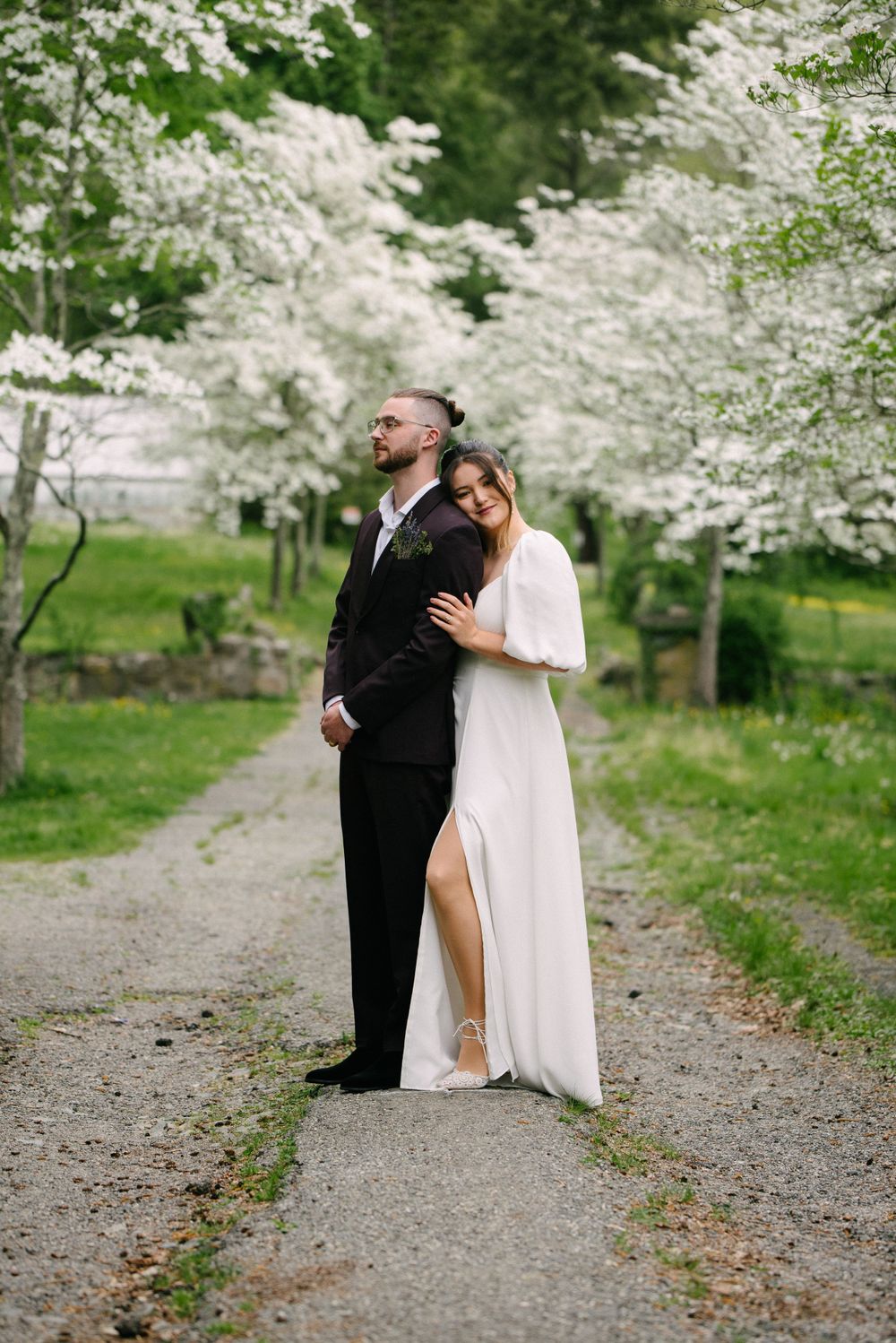 Wedding couple embracing on a path beneath white cherry blossoms in full bloom.