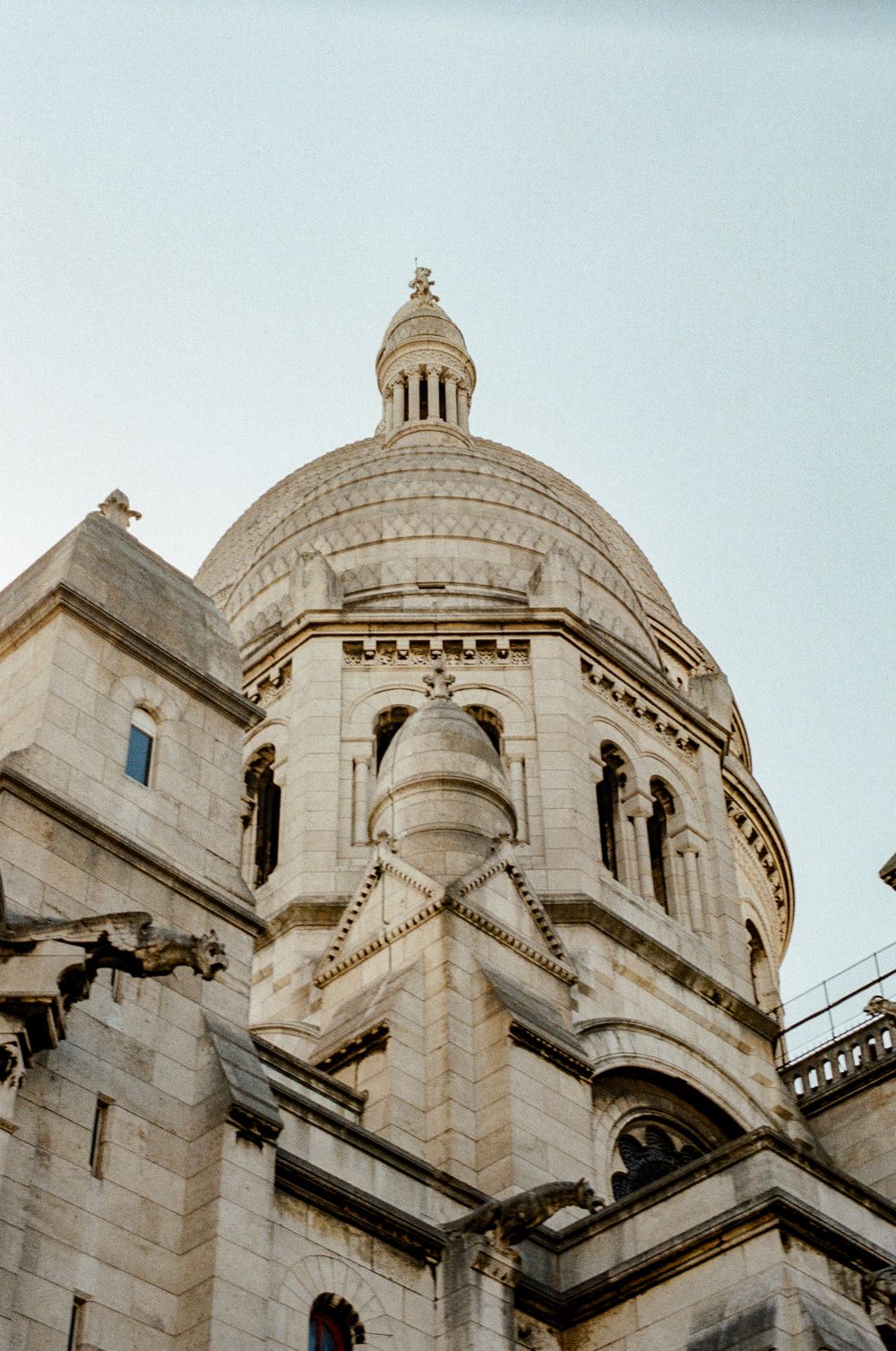 Upward view of Sacré-Cœur Basilica dome in Paris, showcasing ornate white stone architecture against a clear sky.