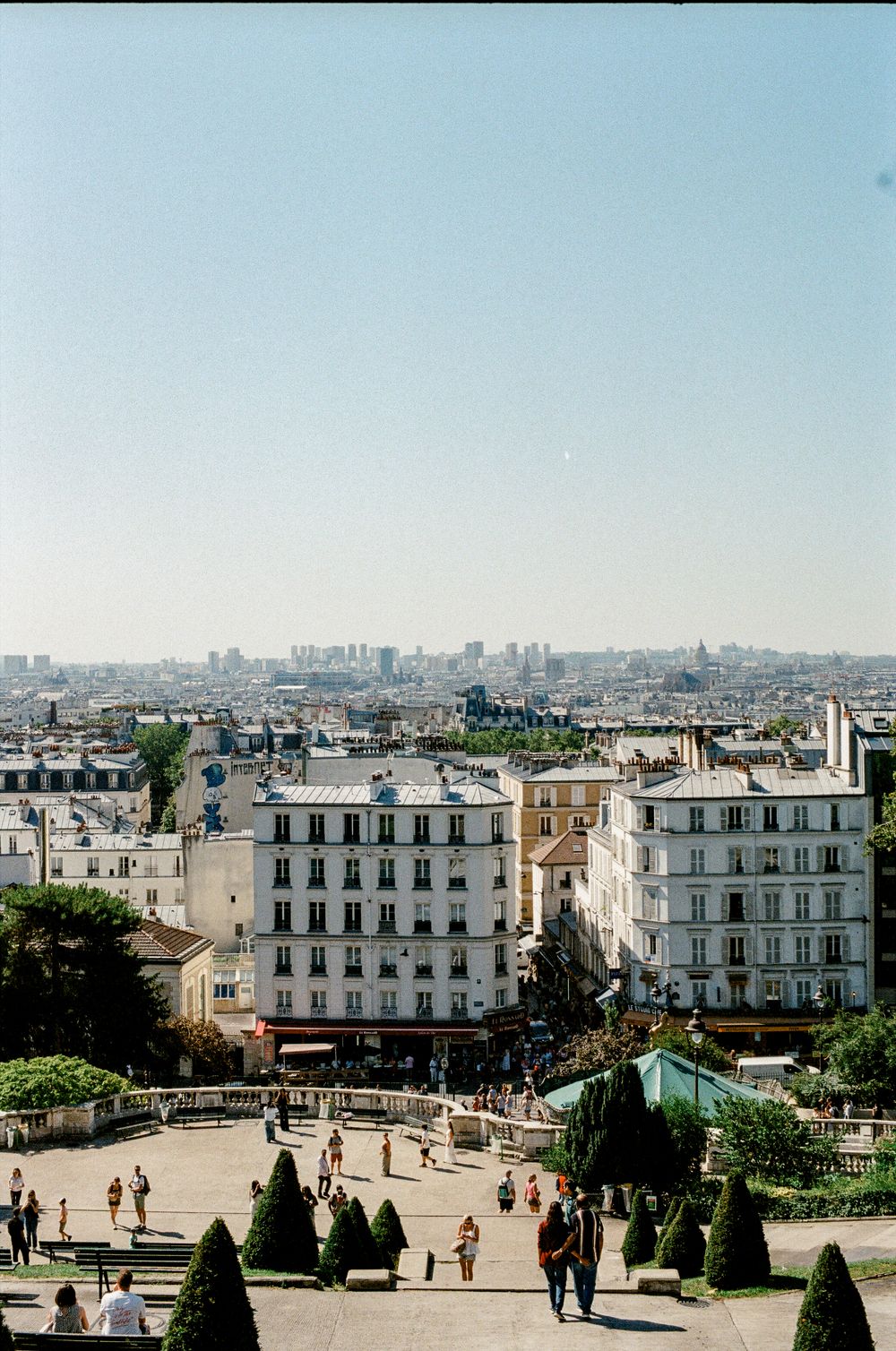 Aerial view of Paris cityscape from Montmartre with Haussmann buildings, manicured gardens, and city skyline on a sunny day.
