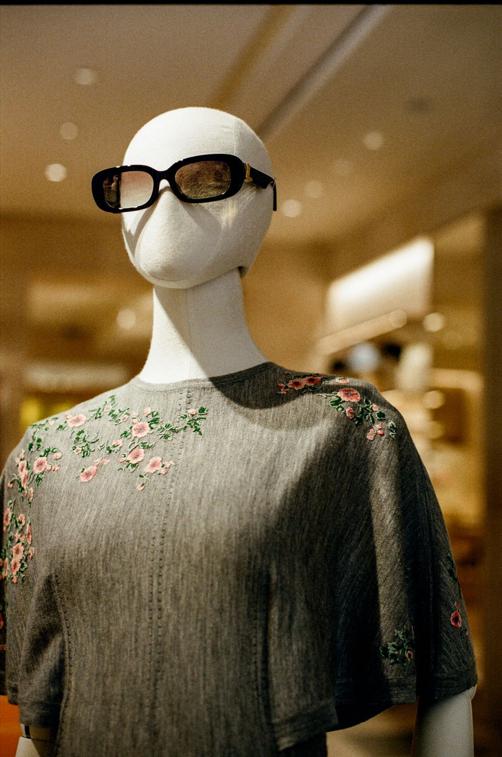 Mannequin wearing gray floral embroidered top and black sunglasses displayed in a retail store.