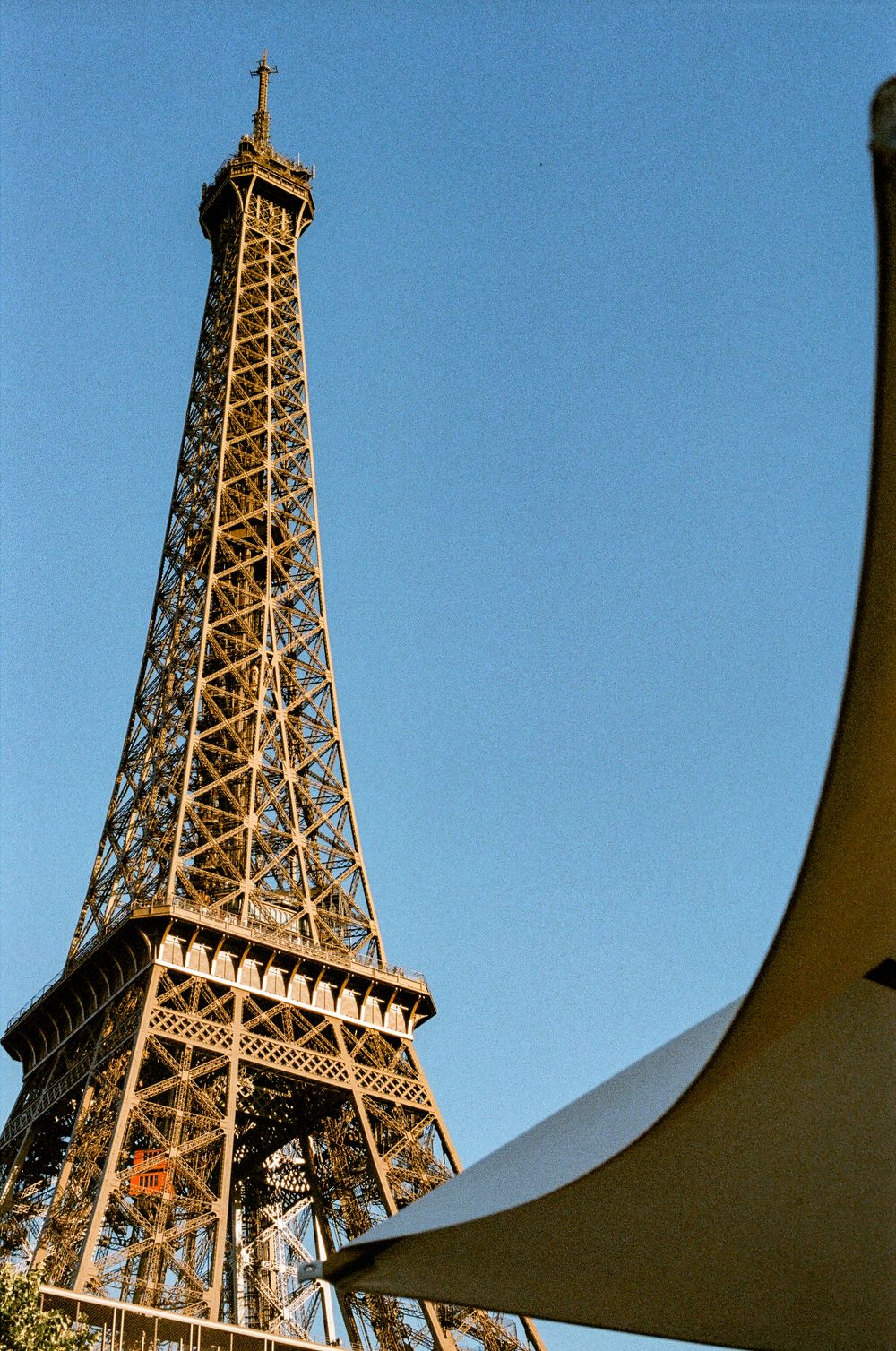The Eiffel Tower rises against a clear blue sky in Paris, France, photographed from a low angle near a white canopy.
