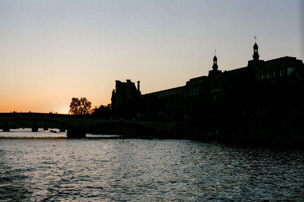 Silhouette of the Louvre Museum and Pont Royal bridge over the Seine River at sunset in Paris, France.