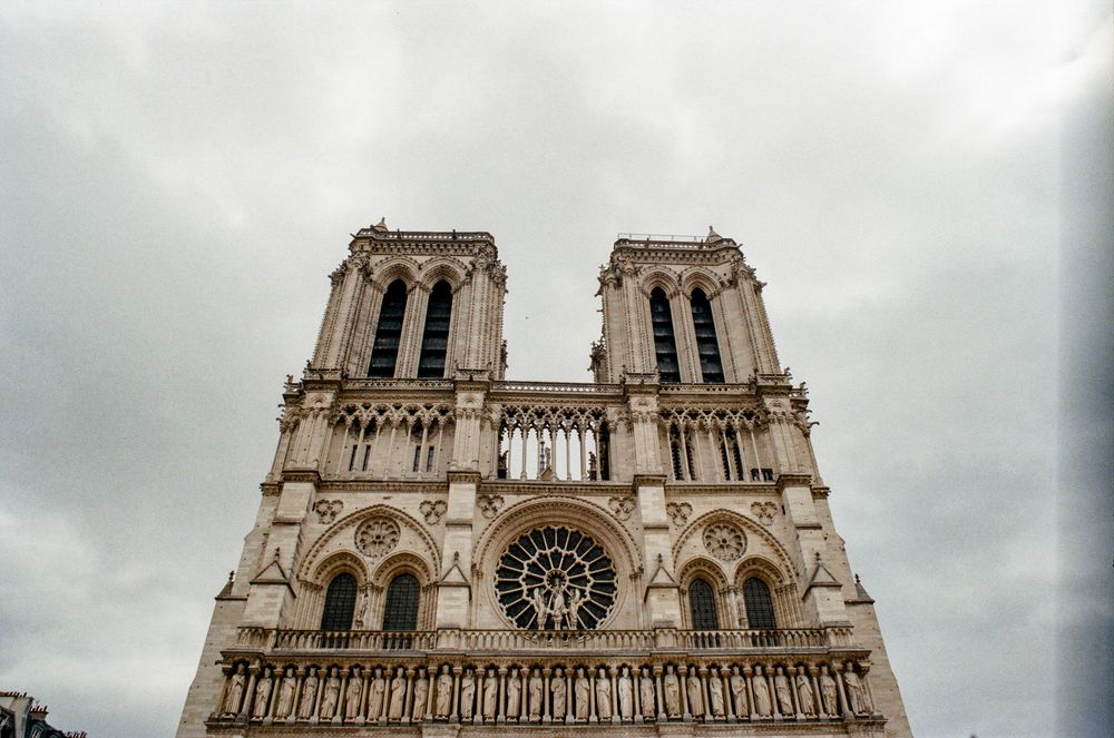 Notre-Dame Cathedral facade in Paris with twin Gothic towers and rose window under cloudy skies.