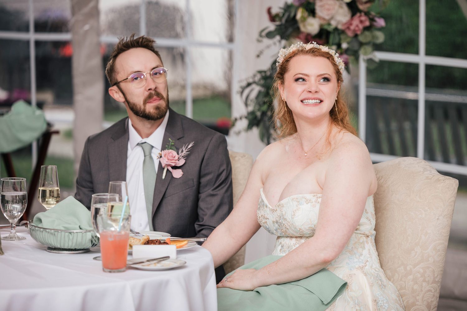 Bride and groom listening to a speech, bride smiling and looking upward.