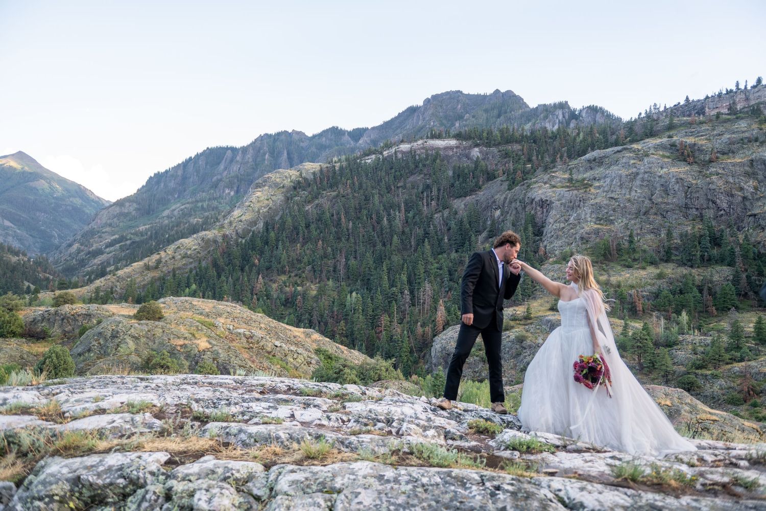 A bride and groom stand together on a mountain ridge with the snow-capped peaks of the San Juan mountains in the distance in the fall.