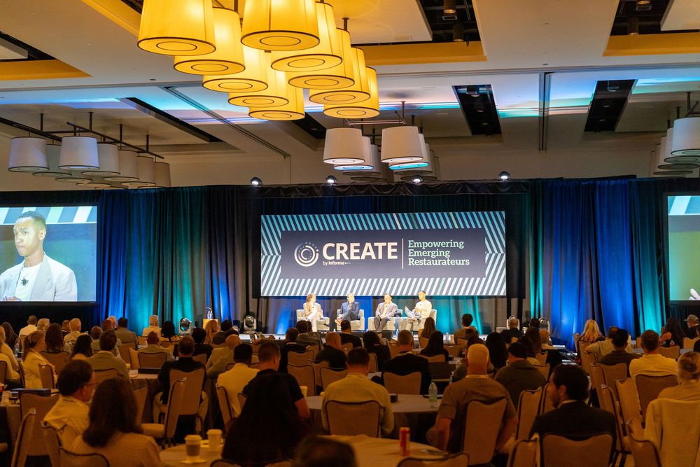 Large conference hall filled with attendees at the CREATE Empowering Innovation Summit on a bright stage.