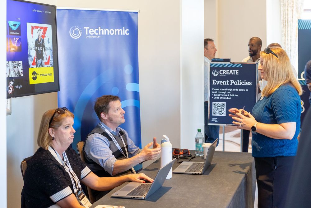 People networking at a Technomic CREATE event registration desk with laptops and event policies sign.