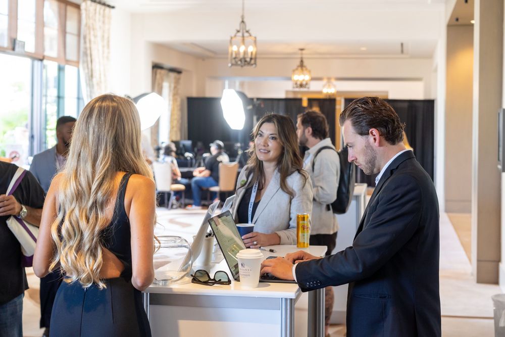 Professionals networking at a corporate event registration desk in an elegant venue with warm lighting.