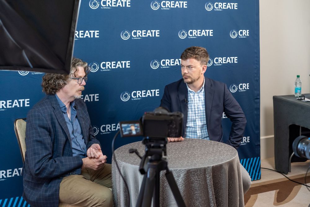 Two professionals engaged in a recorded interview at a CREATE conference event, seated at a round table.