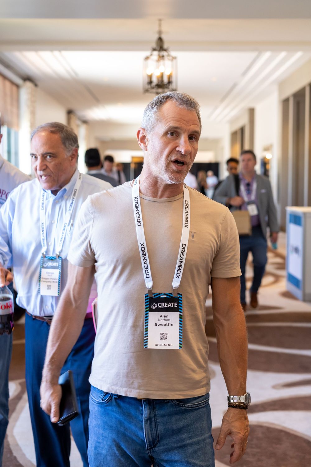 Man wearing CREATE conference badge walking through hotel corridor at industry networking event.