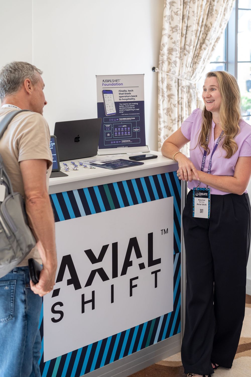 Woman at Axial Shift trade show booth smiling while speaking with a visitor at a professional conference.