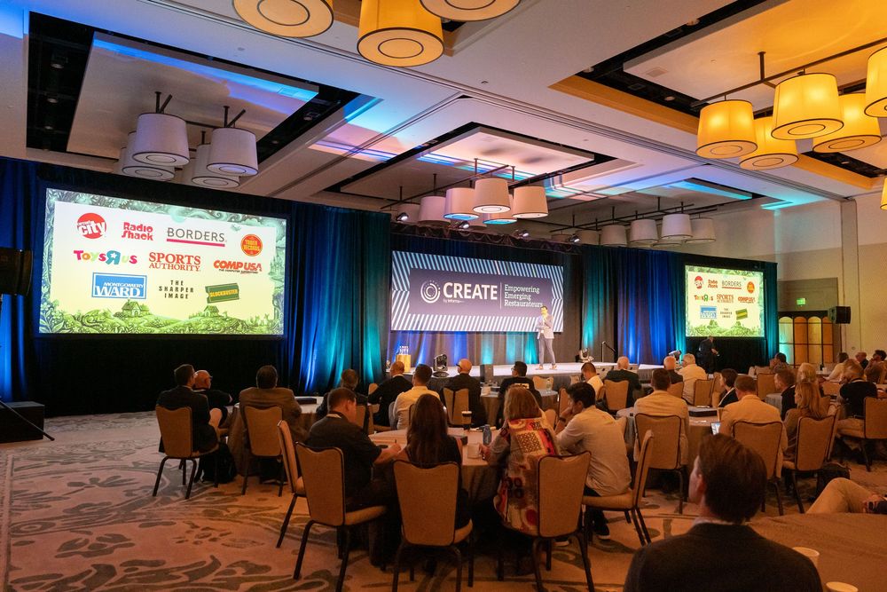 Large conference ballroom with attendees seated at round tables facing a stage with CREATE branding and sponsor logos.