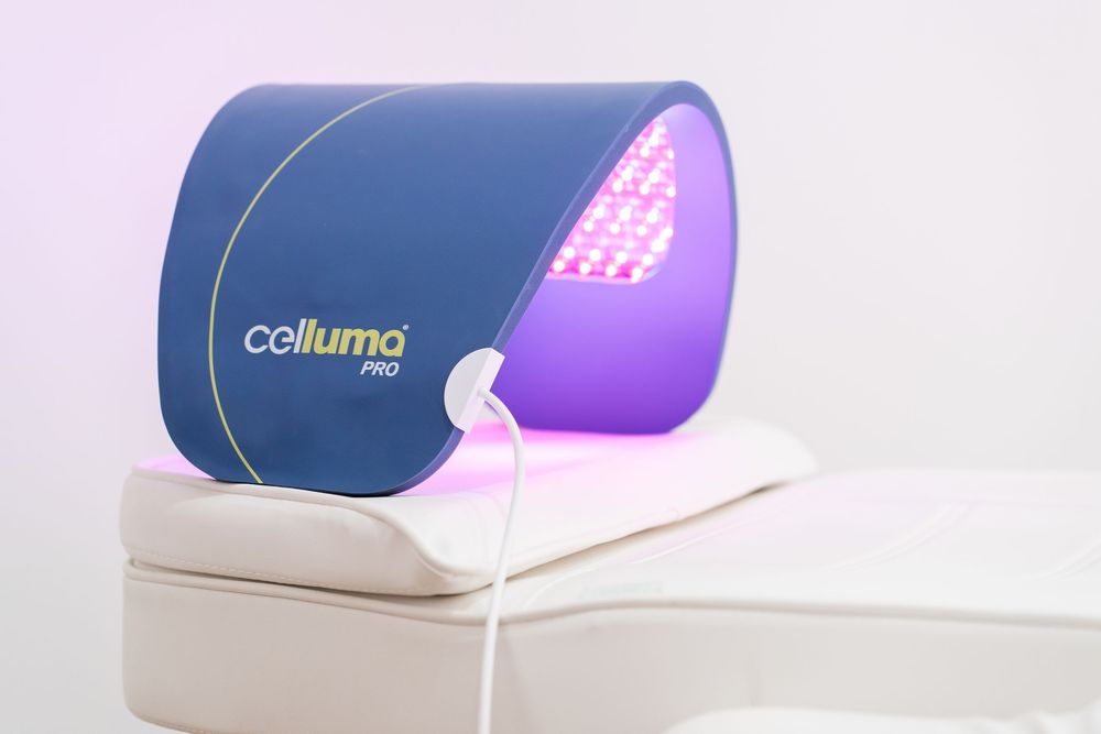 Celluma PRO LED light therapy device glowing purple and red on a white cushion against a light background.