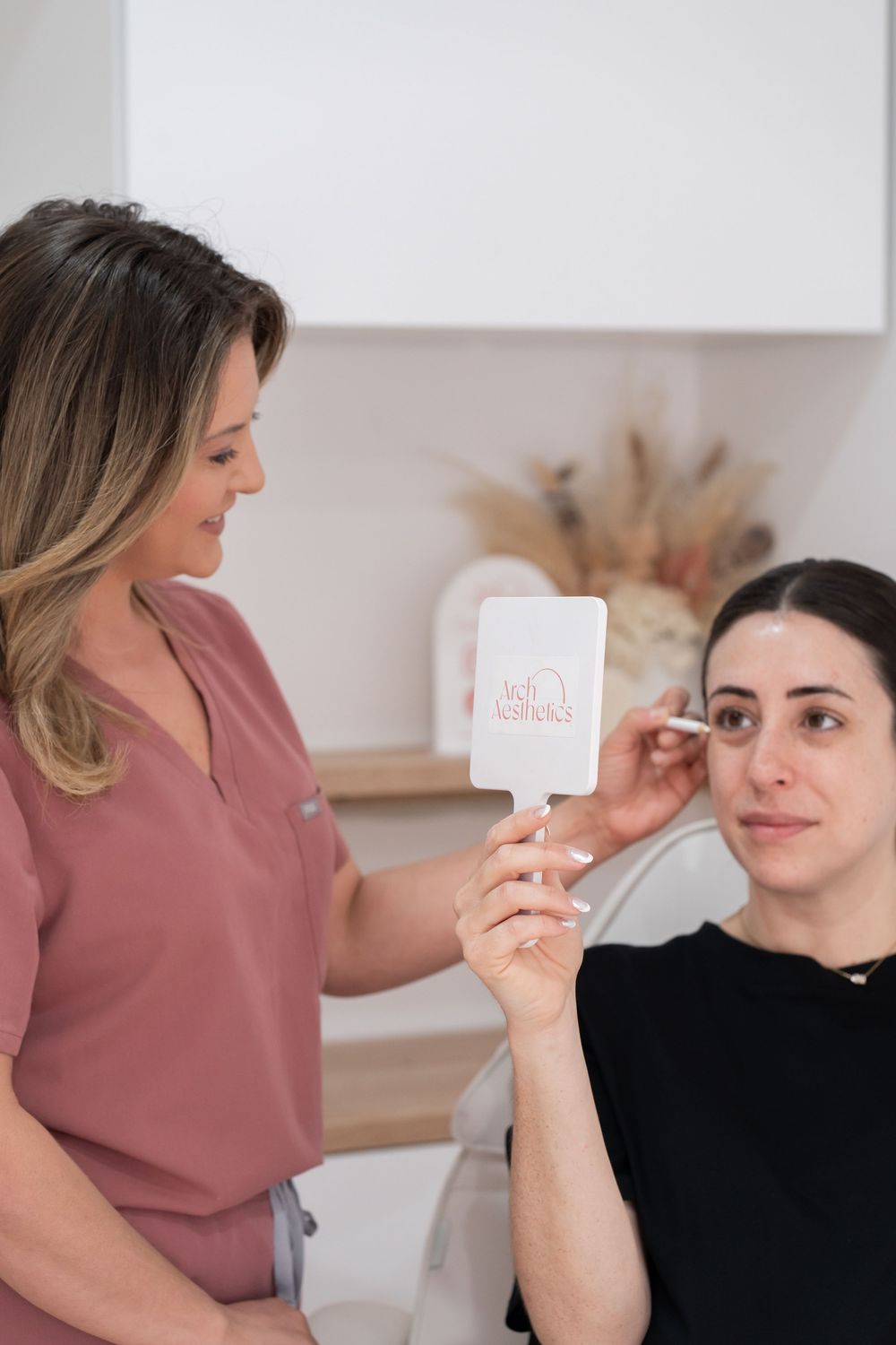 Aesthetician showing a branded mirror to a client during a facial consultation in a modern beauty clinic.
