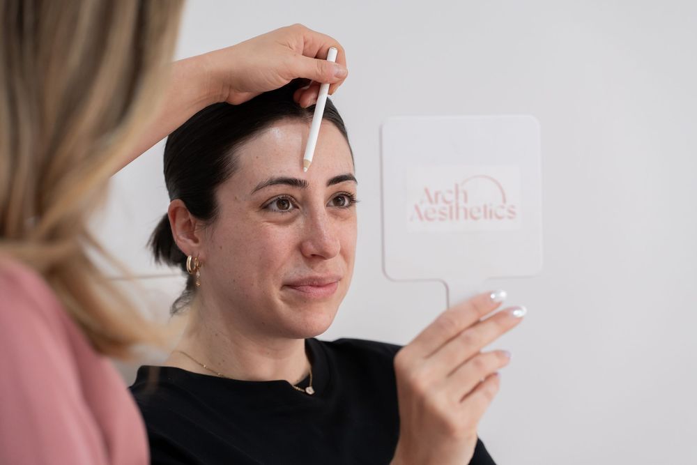 Aesthetician measuring client eyebrows with a ruler at Arch Aesthetics salon during a brow shaping consultation.
