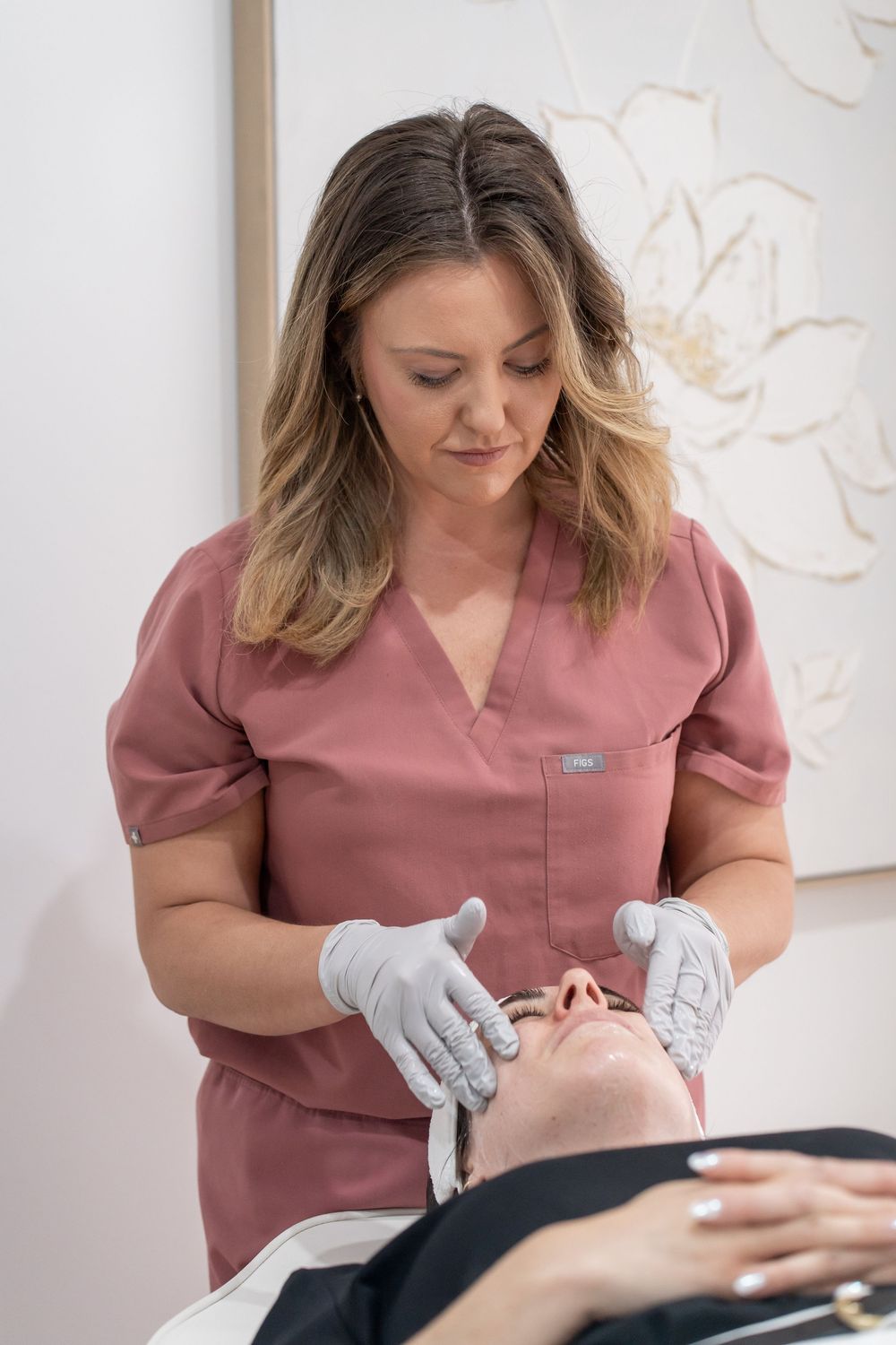 Professional esthetician in pink scrubs performing a facial treatment on a client in a beauty salon.