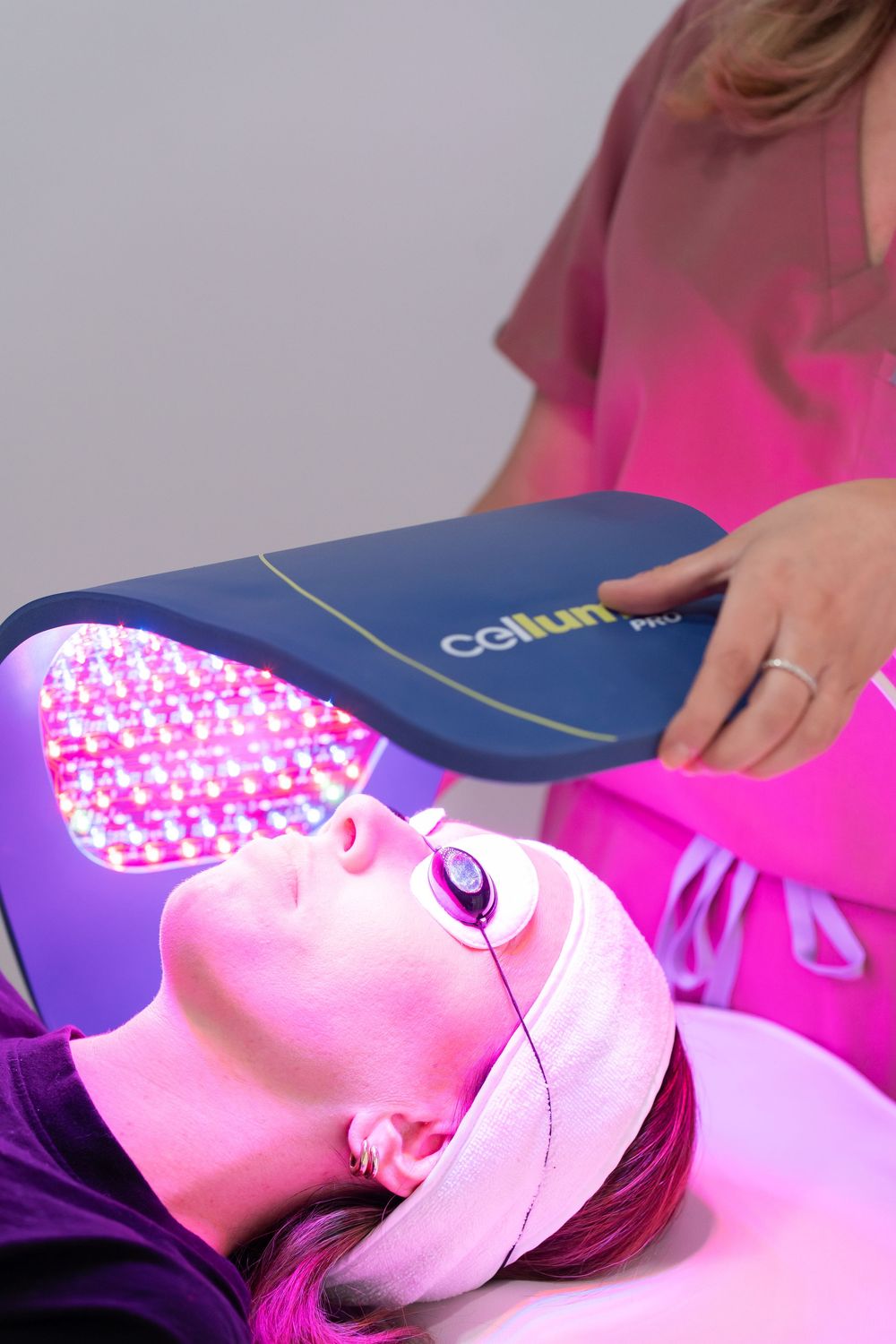 Woman receiving Celluma Pro LED light therapy facial treatment from esthetician in pink scrubs at spa.