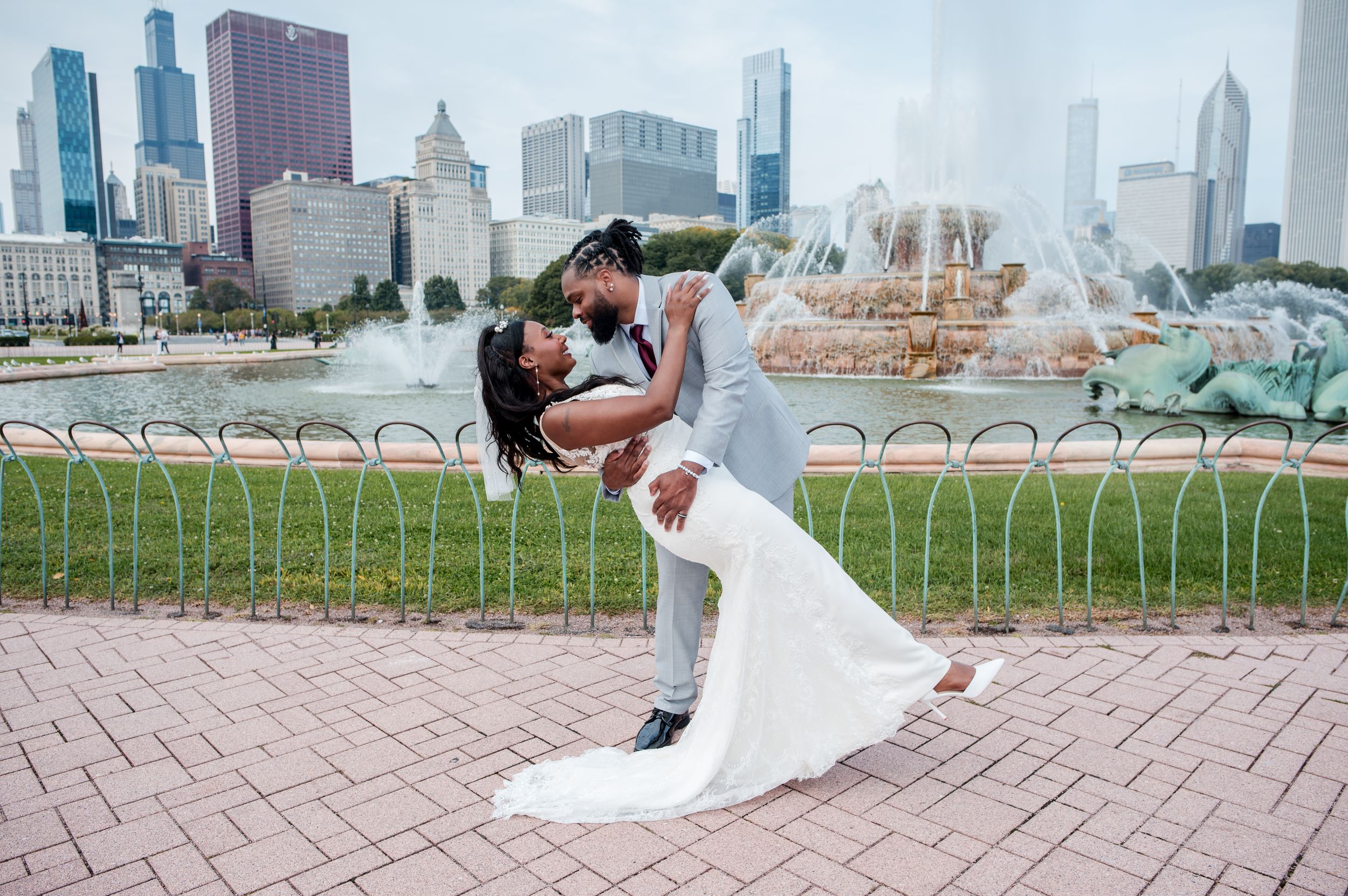 Groom dips bride in white gown near Buckingham Fountain in Chicago with city skyline backdrop.