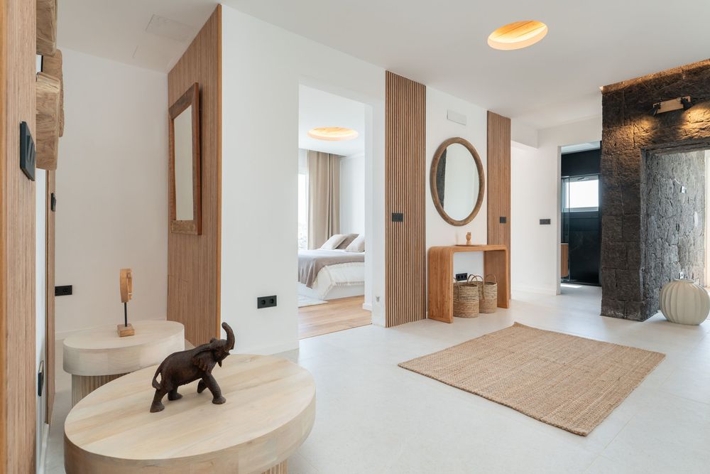 Modern villa hallway with wooden accents, round mirror, elephant decor, and a view into a bright bedroom.