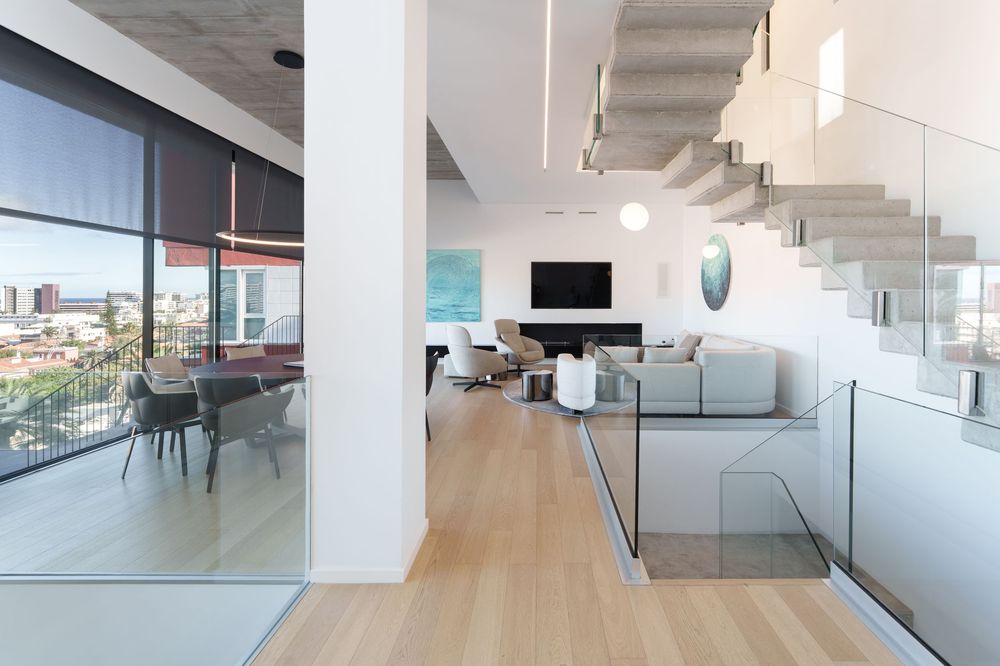 Modern open-plan penthouse interior with glass railings, floating staircase, light wood floors, and contemporary living space.