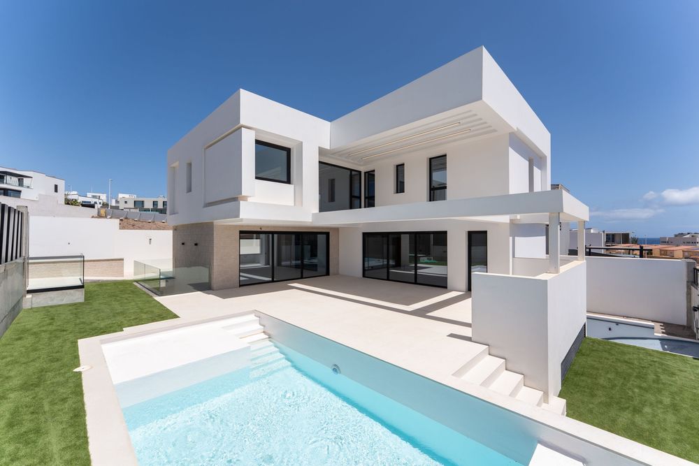 Modern white two-story villa with private pool, glass railings, and manicured lawn under a clear blue sky.