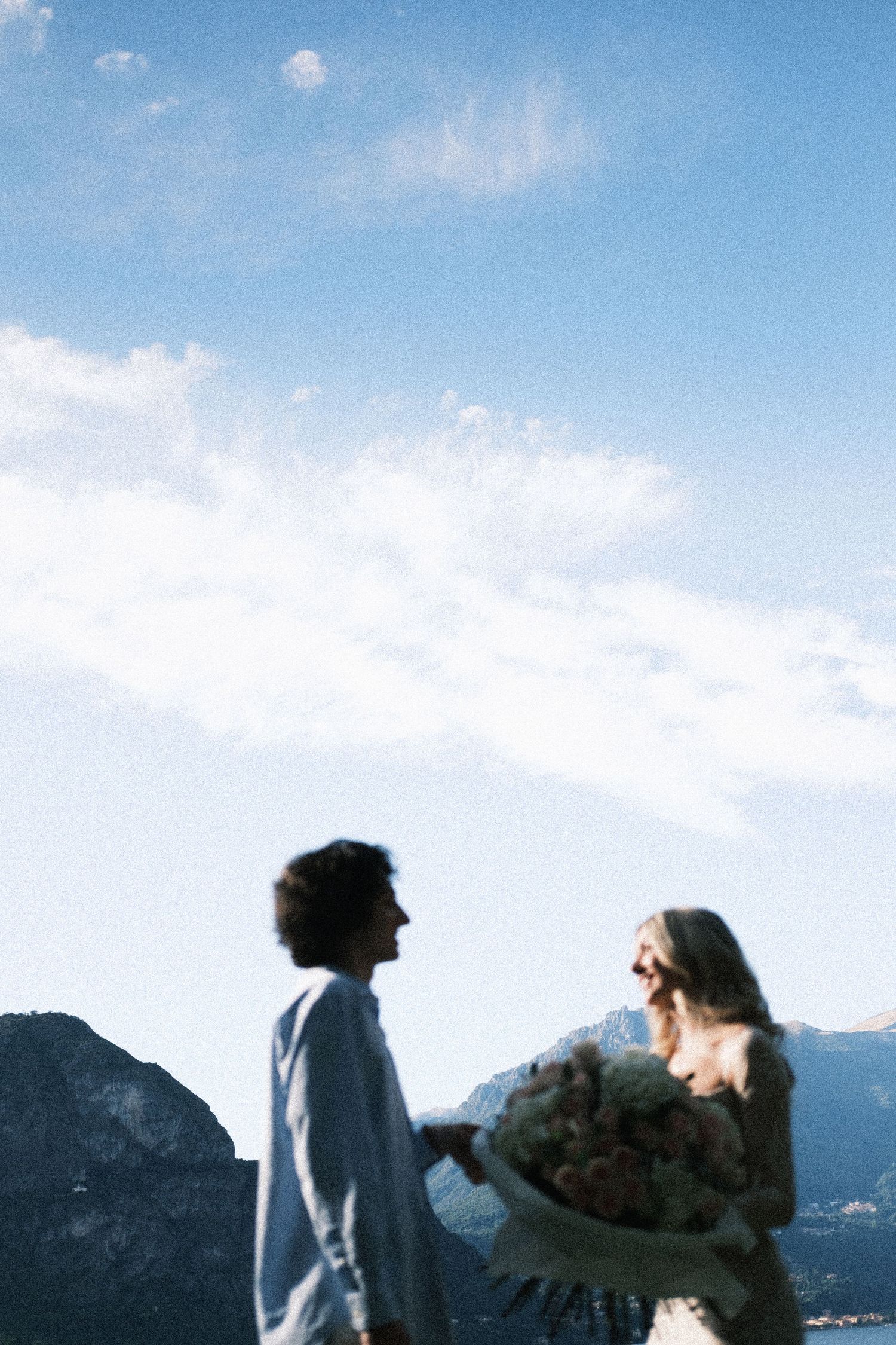 Couple sharing a romantic moment with flowers against a scenic mountain and blue sky backdrop.