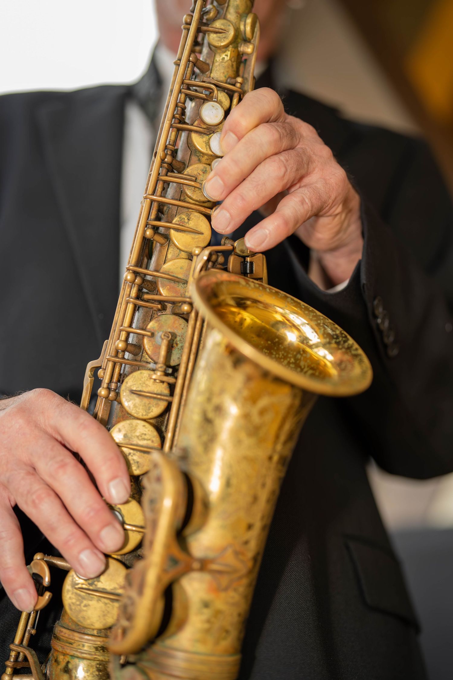 Close-up of a musician's hands playing a golden brass saxophone while wearing a dark suit jacket.